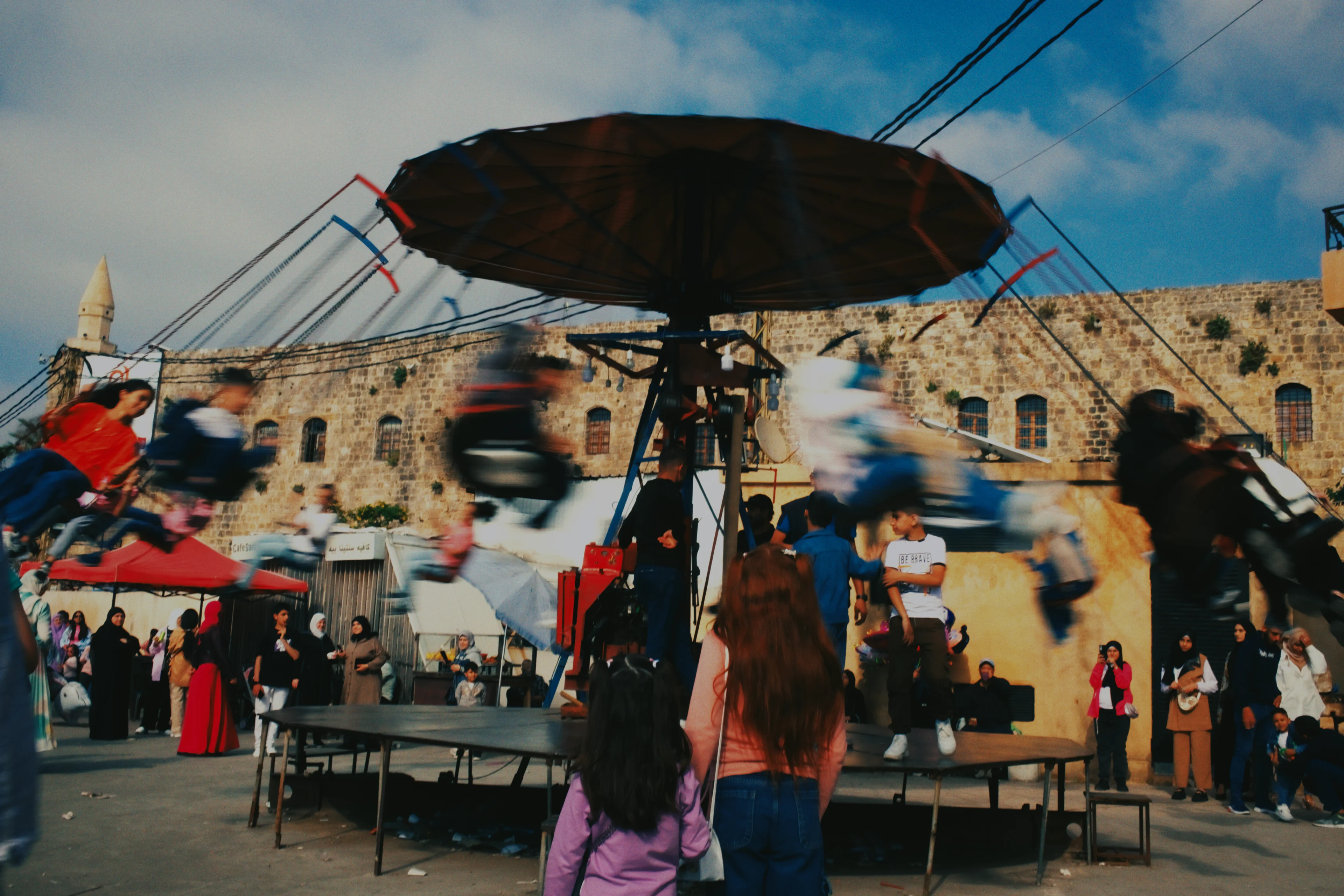 A carousel spinning in front of an old stone wall, developed on Fuji Pro 800Z